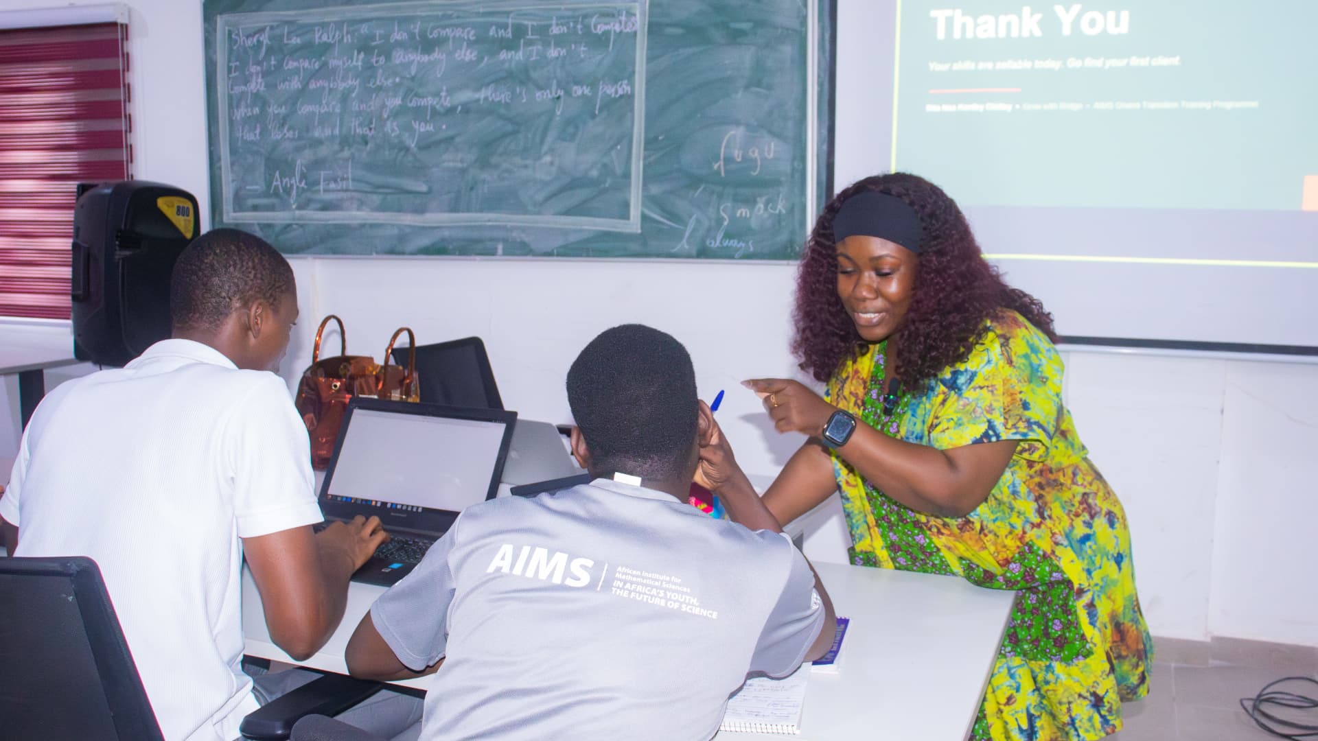 Rita working one-on-one with participants at their laptops during an AIMS Ghana training session
